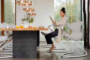 Young lady sitting reading a paper on an Aeris Oyo at home. 6 Oyo's around the dinning table. Oyo in light grey melange on a white frame